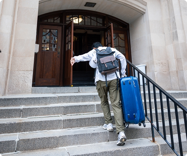 A student carrying a suitcase up a flight of stairs
